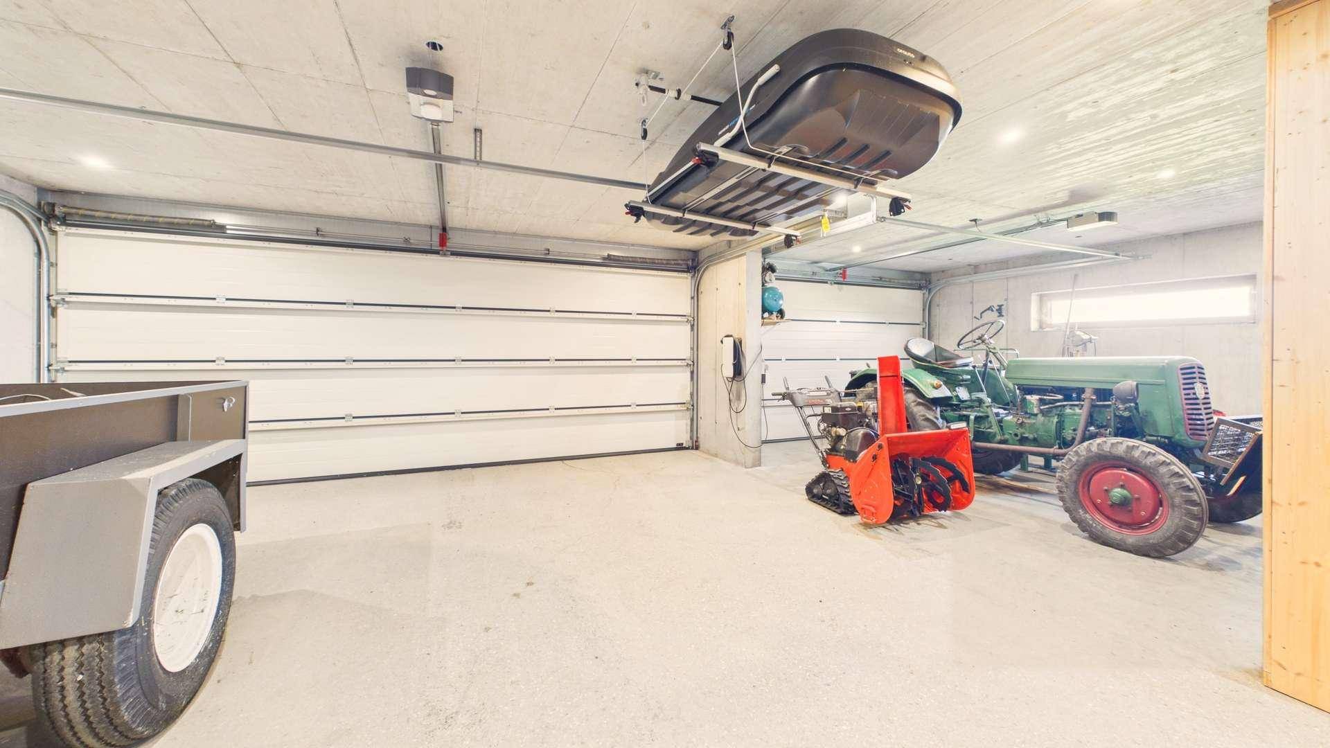 Große Garage mit zwei Toren, einem Anhänger, Traktor und Schneepflug.