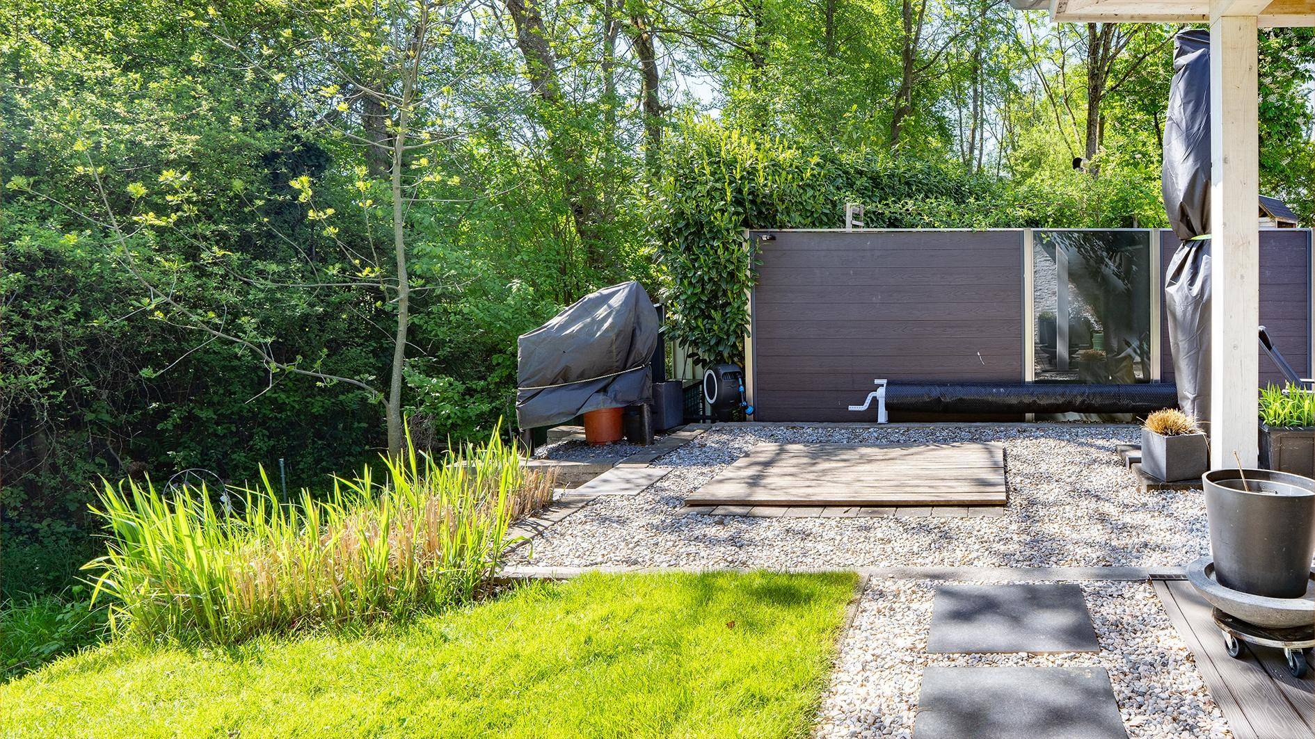 Hinterer Gartenbereich mit Kiesfläche, Holzdetails und umgeben von dichtem Grün.