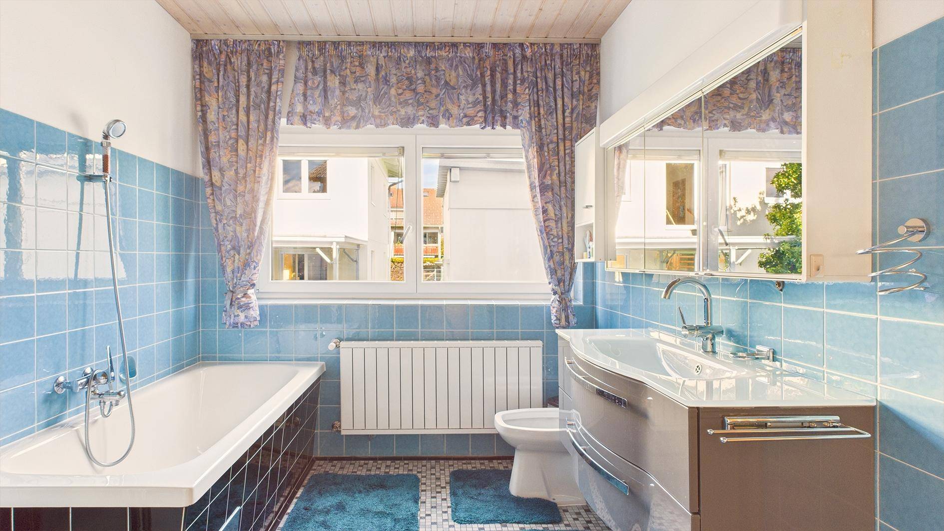 Badezimmer im Stil der 80er Jahre mit blauen Fliesen, Badewanne und Fenster.