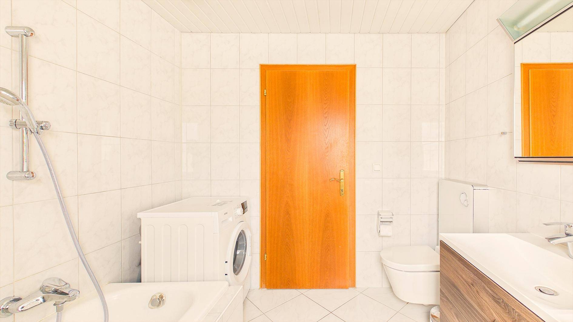 Funktionales Badezimmer mit Badewanne, Toilette, Waschmaschine und weißen Fliesen.