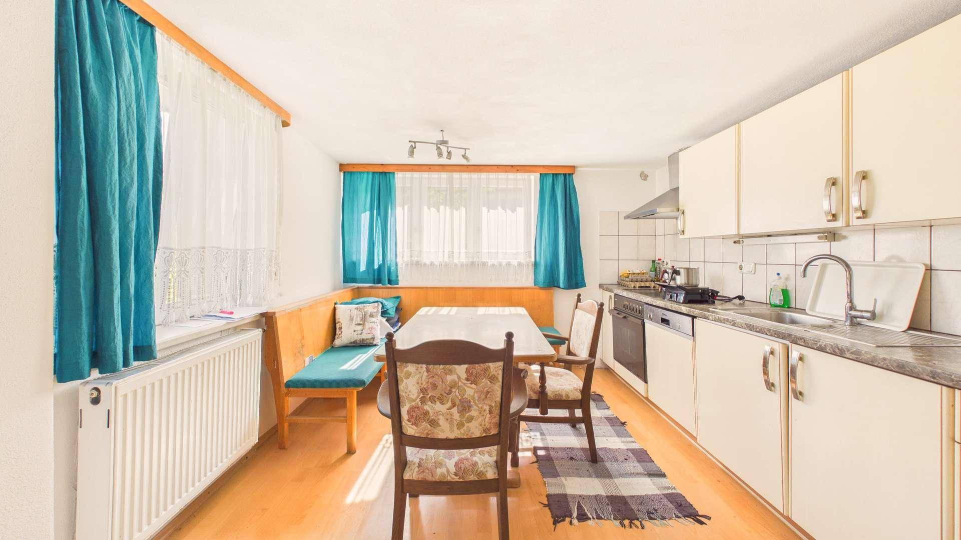 Helle Wohnküche mit weißer Einbauküche, Esstisch und Sitzbank am Fenster.