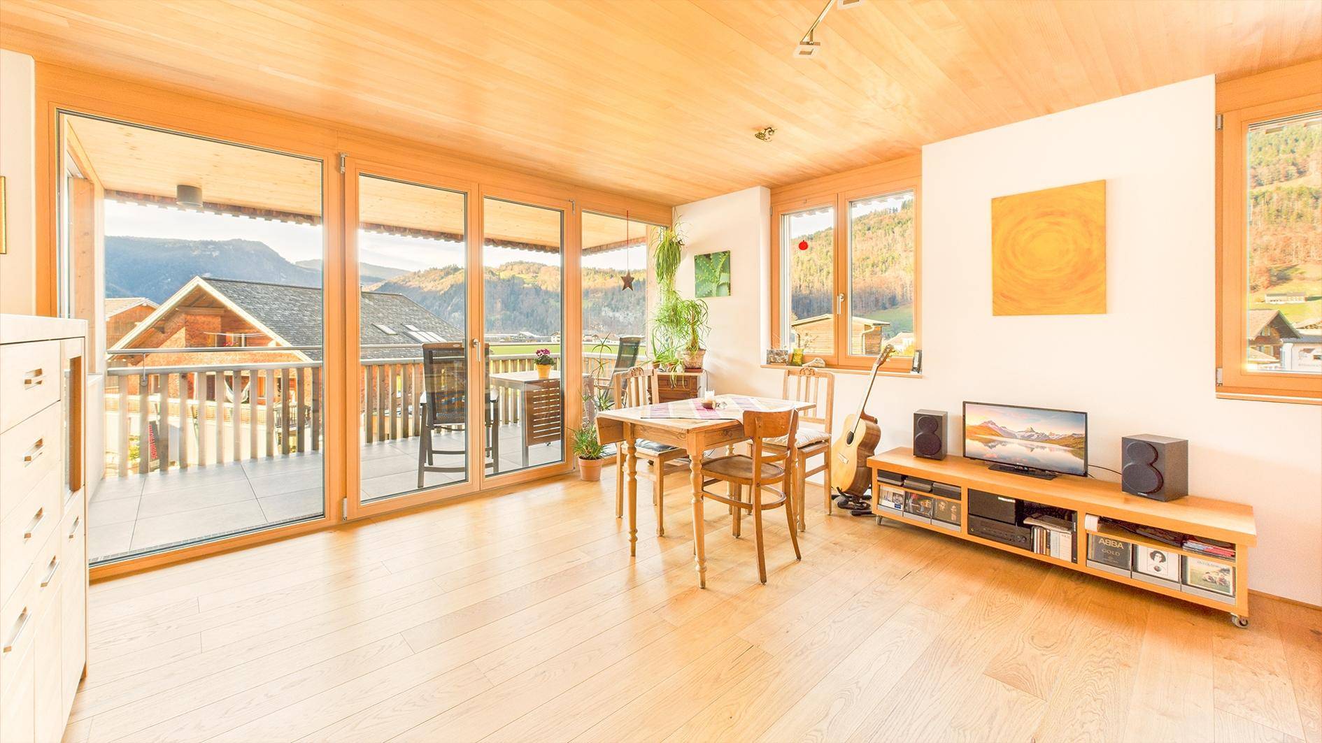 Lichtdurchfluteter Wohnbereich mit Esstisch, Holzboden und Zugang zum Balkon mit Bergsicht.