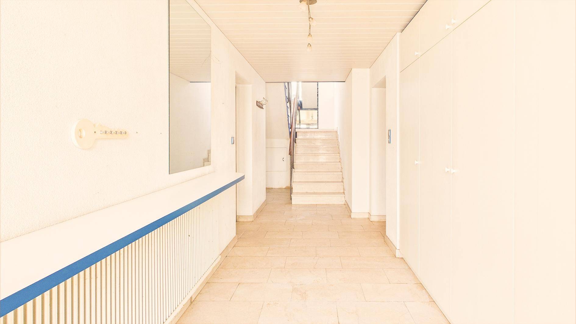 Heller Flur mit Fliesenboden, weiß gestrichenen Wänden und Treppenaufgang zum Obergeschoss.
