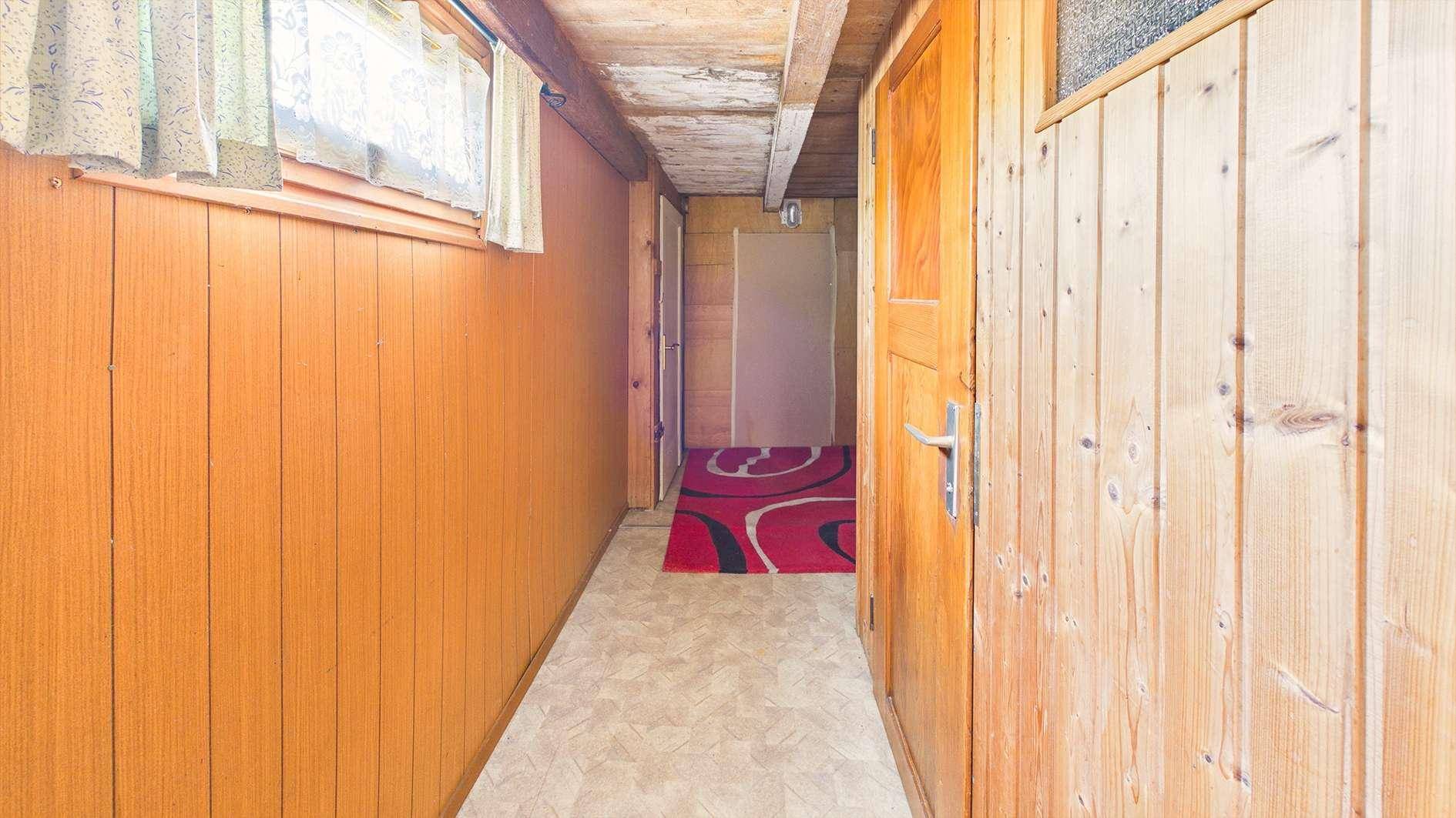 Schmaler Flur mit Holzvertäfelung an den Wänden und einem Fenster am Ende.