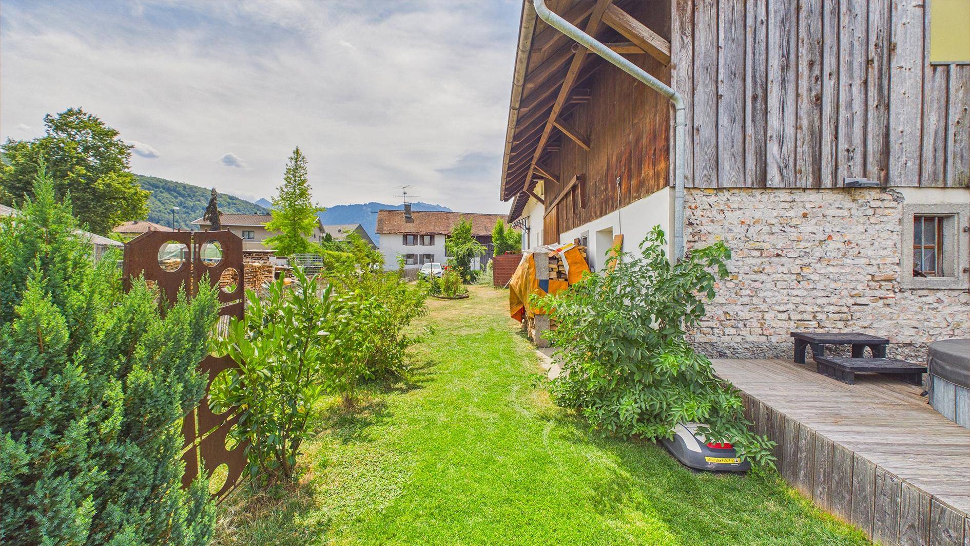 Gartenansicht mit Rasenroboter, Sträuchern und der Holzfassade des Scheunengebäudes.