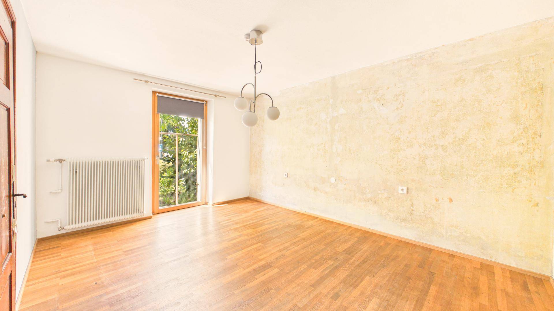 Geräumiges Wohnzimmer mit Holzboden, Fenster und Heizkörper, bereit zur Renovierung.