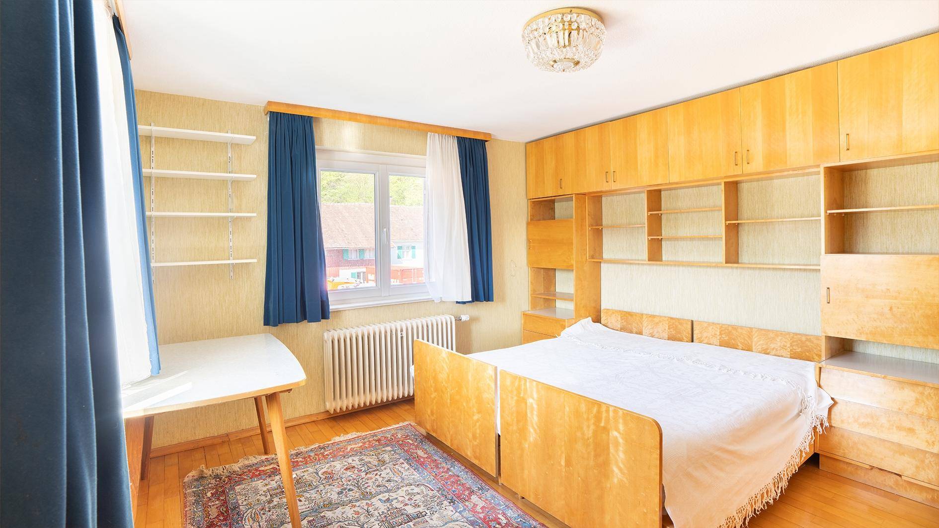 Gemütliches Schlafzimmer mit Holzbett, Einbauschränken und blauen Vorhängen.