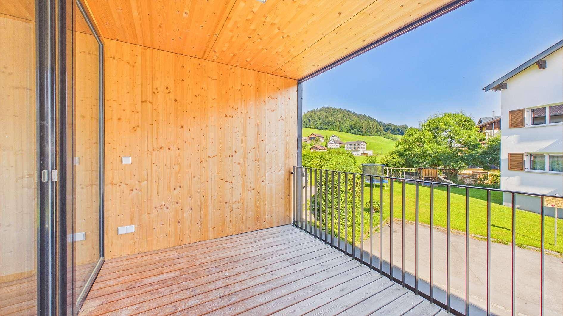 Geräumiger Balkon mit Holzboden und schöner Aussicht auf die grüne Landschaft und umliegende Häuser.