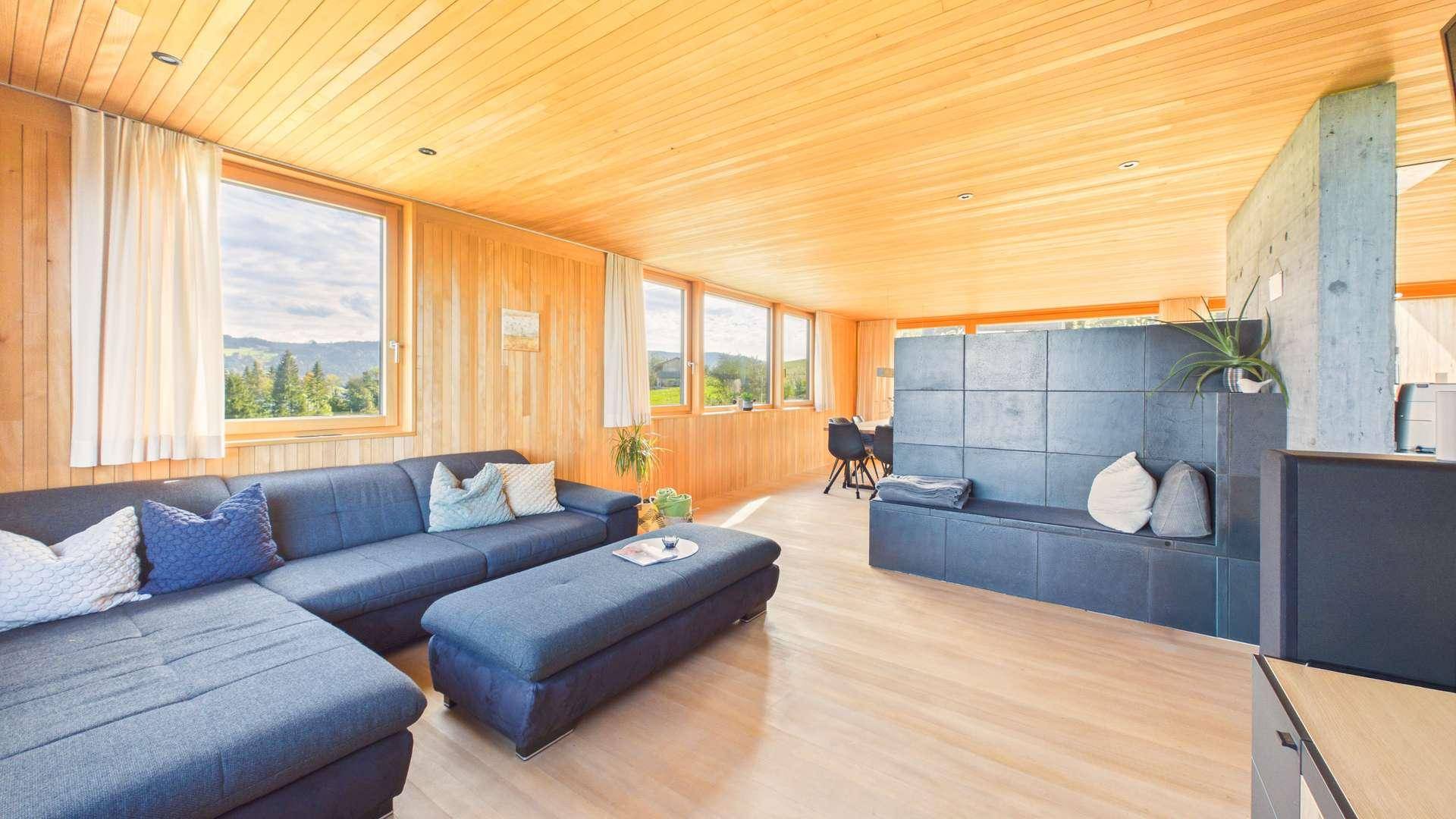 Gemütliches Wohnzimmer mit großem Sofa, Holzwänden und weitem Blick auf die grüne Landschaft.