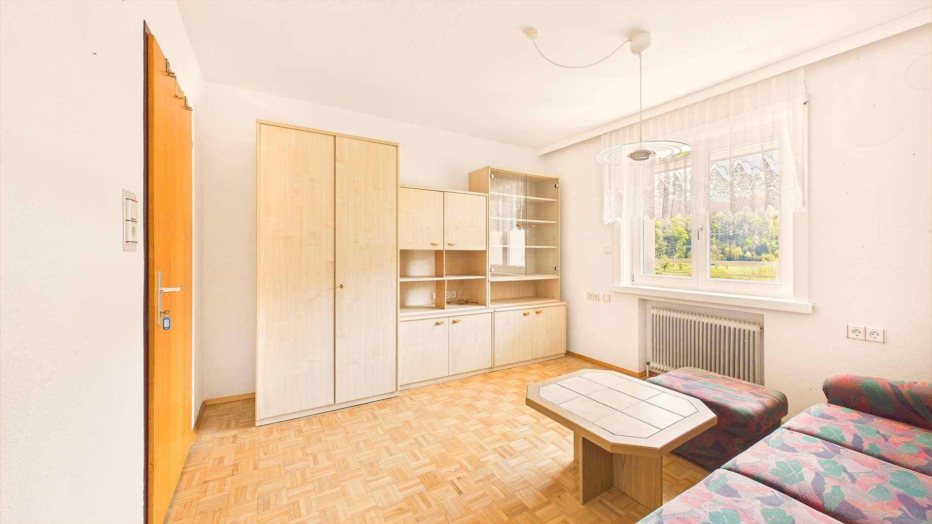 Helles Zimmer mit Parkettboden, Schrankwand und Holztür.