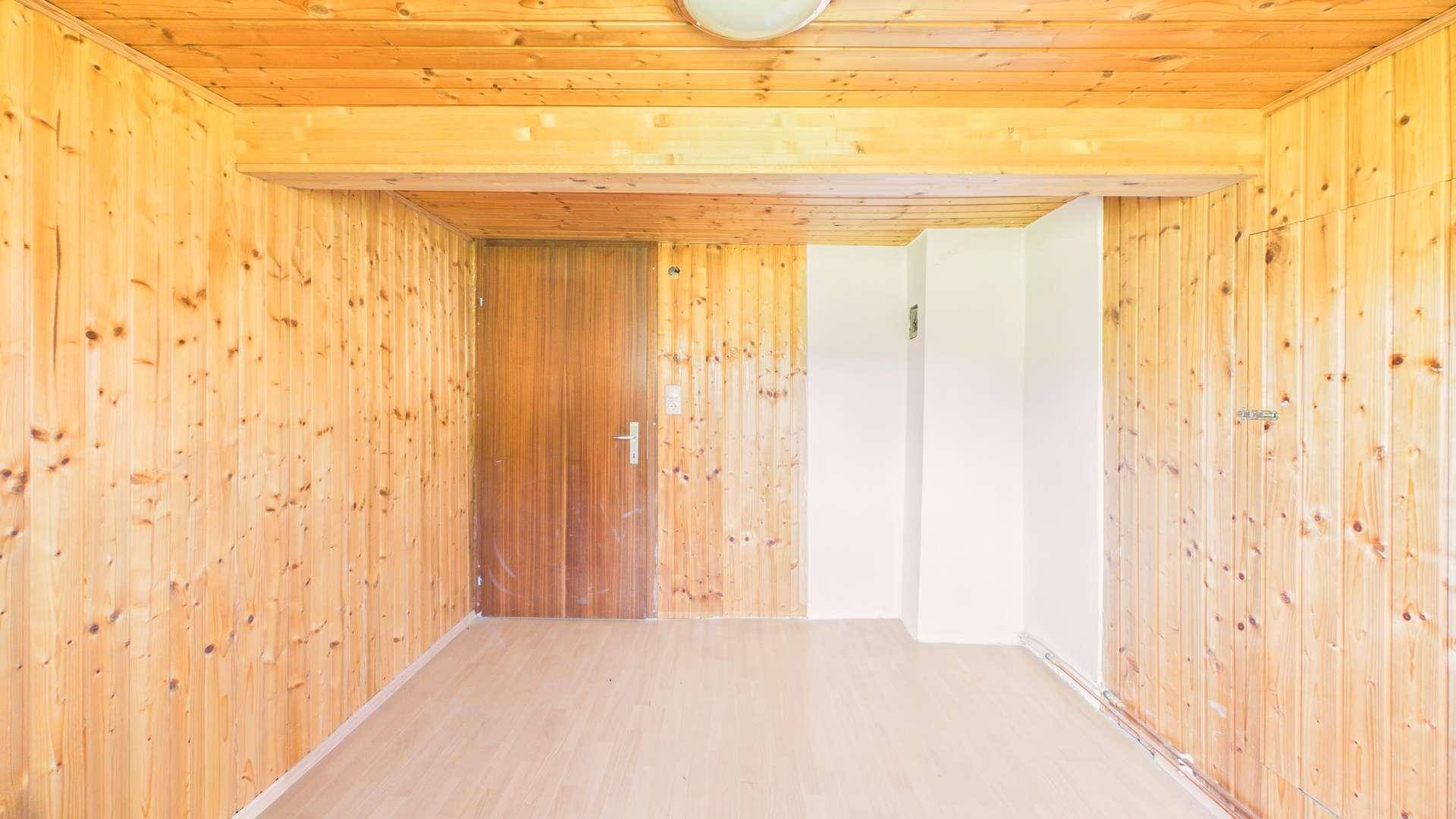 Geräumiger Raum mit Holzverkleidung, Holzbalken und einer Tür, bereit zur Einrichtung.