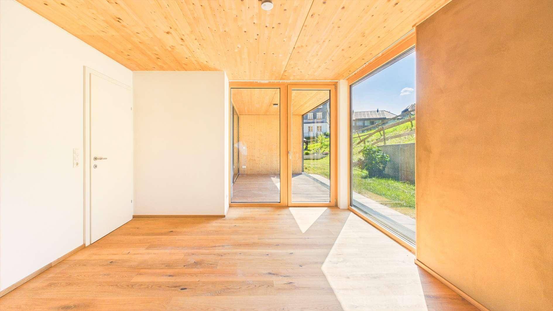 Heller, leerer Raum mit Holzboden und Holzlamellendecke, ausgestattet mit großen Fenstern für viel Tageslicht.