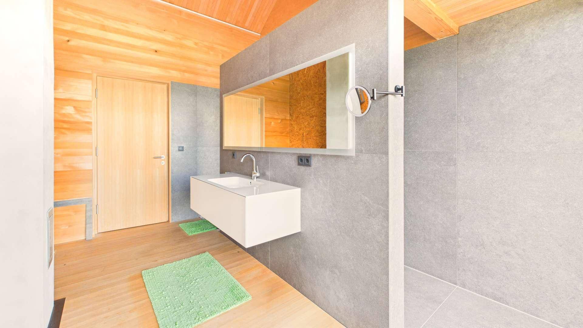 Modernes Badezimmer mit Holzboden, grauen Fliesen und schwebendem Waschtisch.
