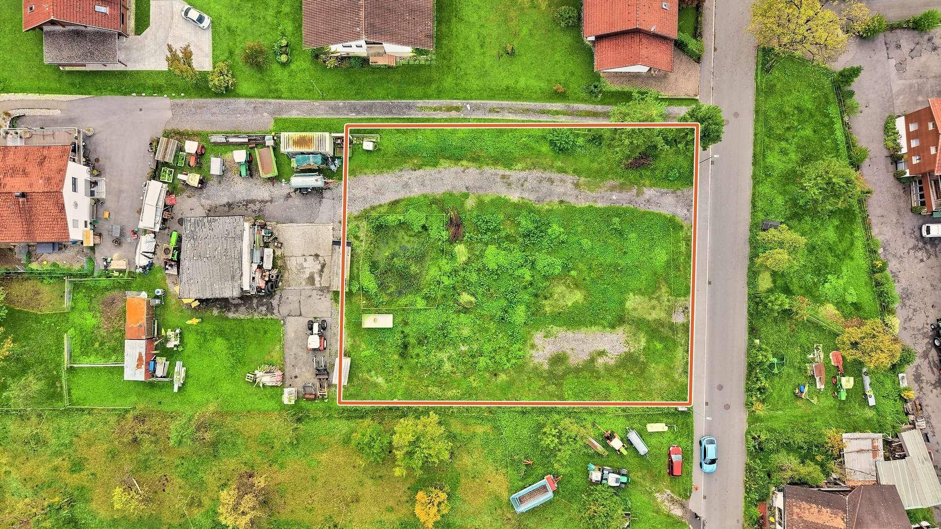 Luftaufnahme eines unbebauten Grundstücks mit roter Umrandung, umgeben von Wohnhäusern und einer Straße.