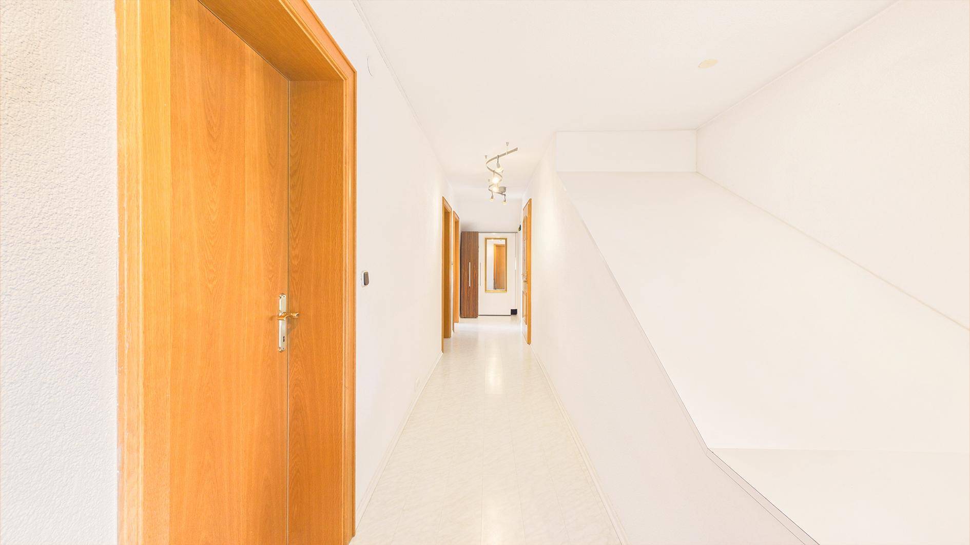 Geräumiger Flur mit Treppenaufgang, Holztüren und heller Beleuchtung.