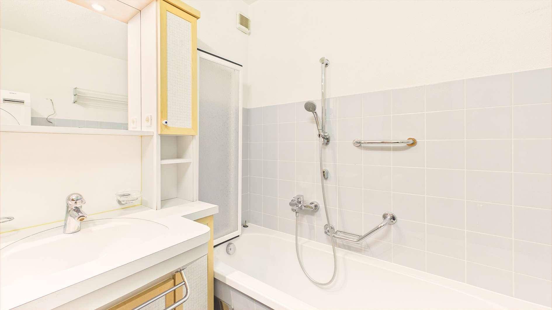 Badezimmer mit Badewanne, Duschvorrichtung und Haltegriffen für mehr Sicherheit.