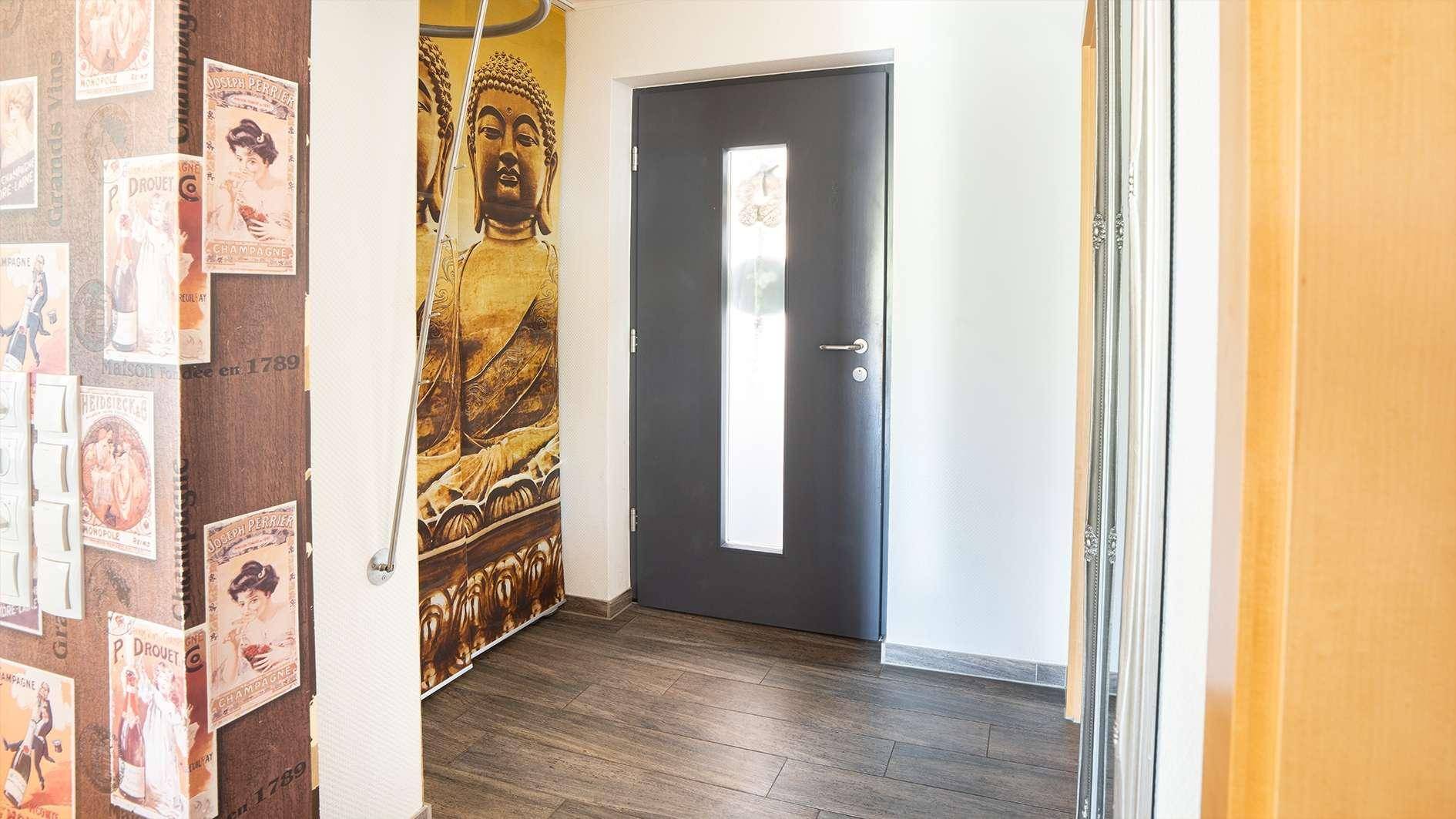 Heller Eingangsbereich mit dunkler Tür, dekorativer Tapete und Holzboden.