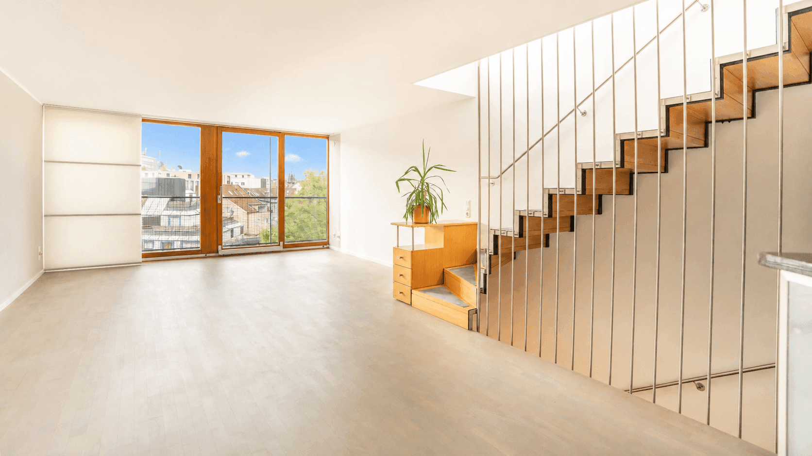 Heller Wohnbereich mit Holztreppe, großen Fenstern und Blick auf die umliegende Stadtlandschaft.
