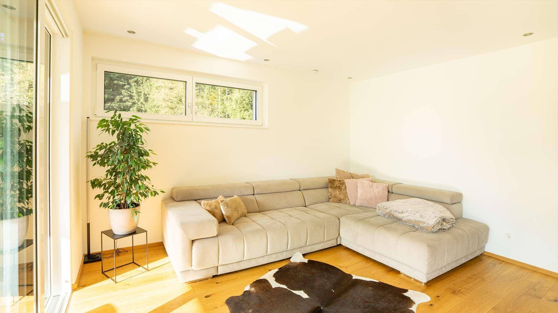 Gemütliches Wohnzimmer mit großem Ecksofa, Holzboden und viel Tageslicht.