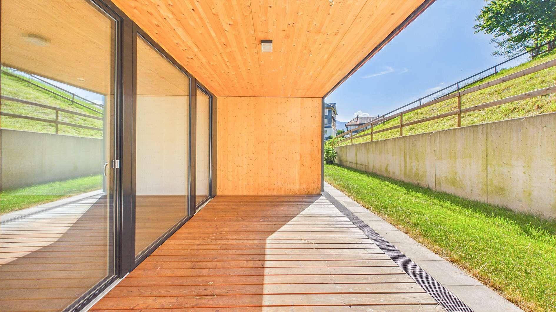Geräumige Holzterrasse mit direktem Zugang zum Garten und Blick auf die grüne Umgebung.