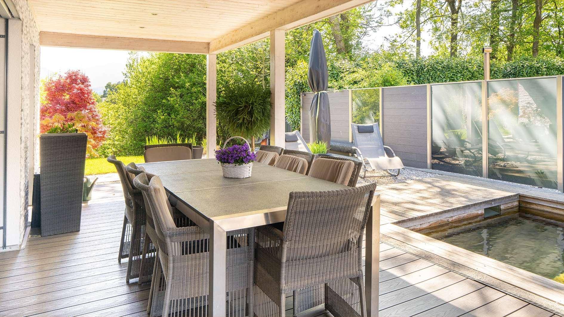 Überdachte Terrasse mit großem Esstisch und Blick auf den Garten und den dekorativen Teich.