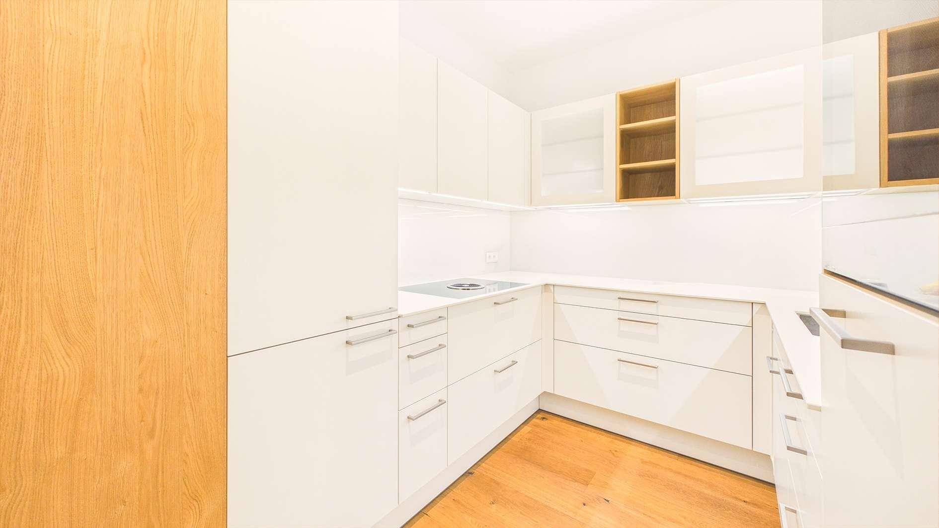 Moderne weiße Küche mit Holzboden, Einbauschränken und integriertem Kochfeld.
