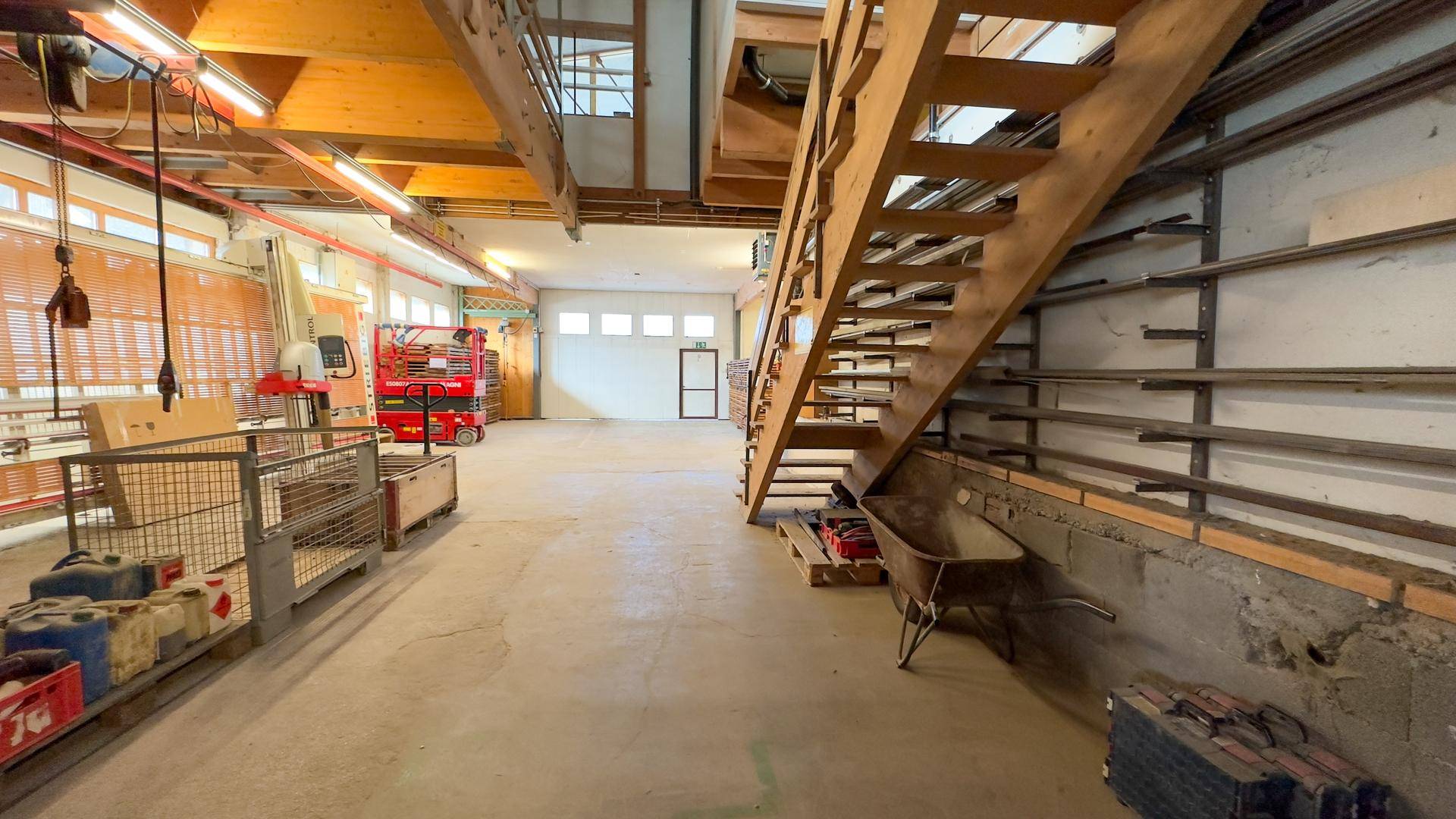 Großer Lagerraum mit Betonboden, einer Holztreppe und Regalen, bereit für die Nutzung.