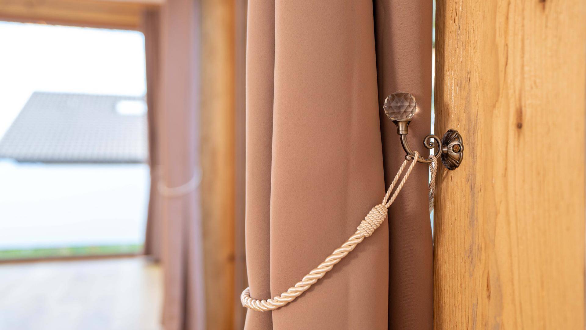 Detailaufnahme eines Vorhangs mit eleganter Raffhalterung und Blick nach draußen.