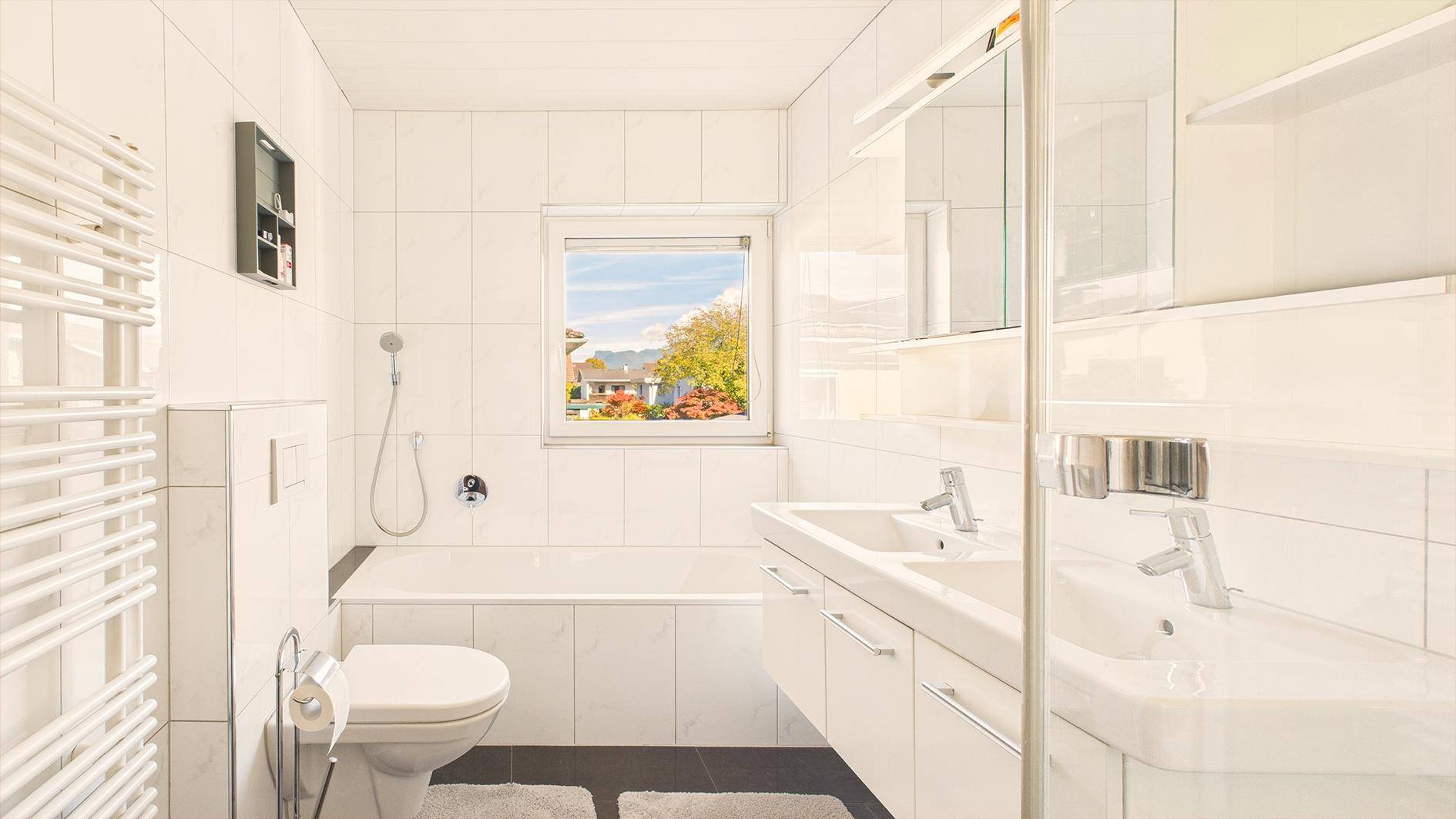 Modernes Badezimmer mit weißen Fliesen, Badewanne, Doppelwaschbecken und Fenster.
