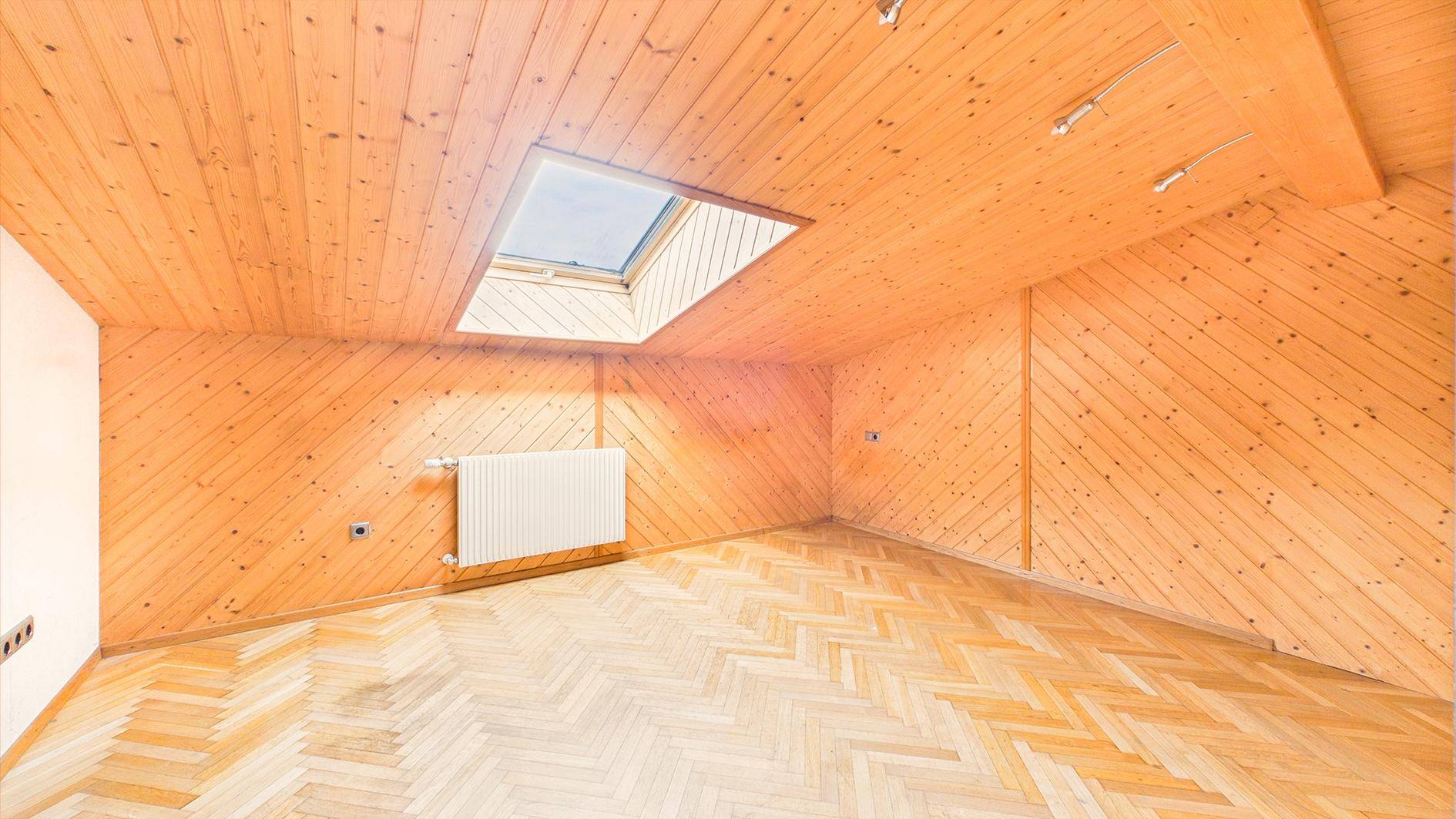 Geräumiges Dachzimmer mit Holzverkleidung, Fischgrätparkett und einem hellen Dachfenster.