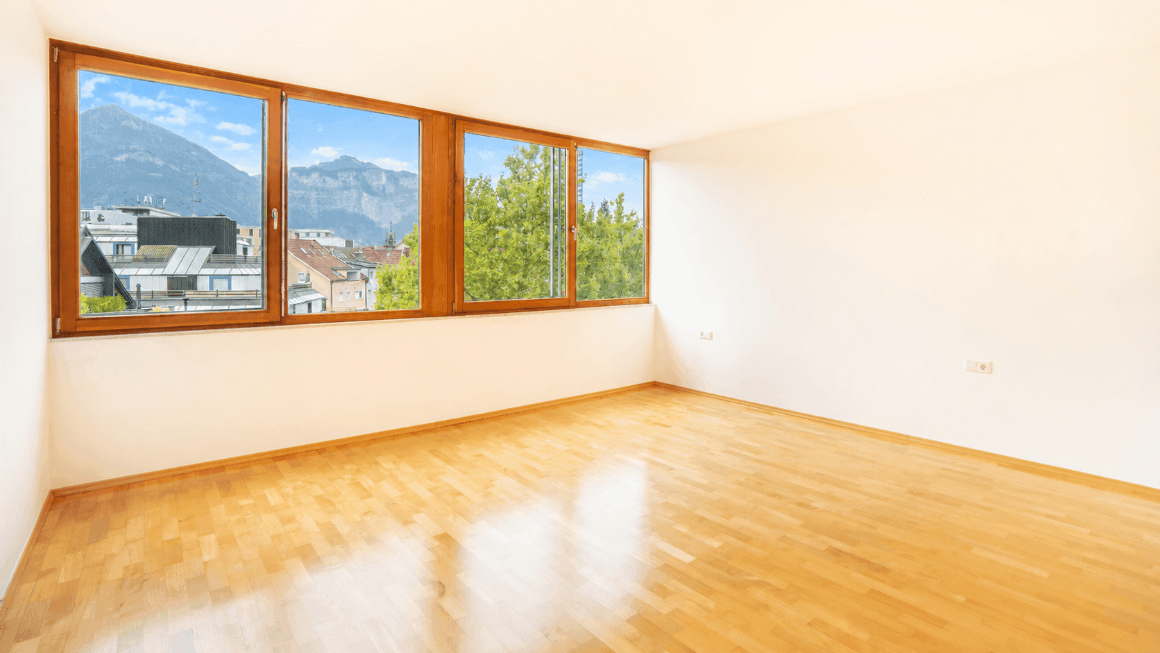 Helles Schlafzimmer mit Parkettboden und großen Fenstern, die einen schönen Blick auf die Berge bieten.
