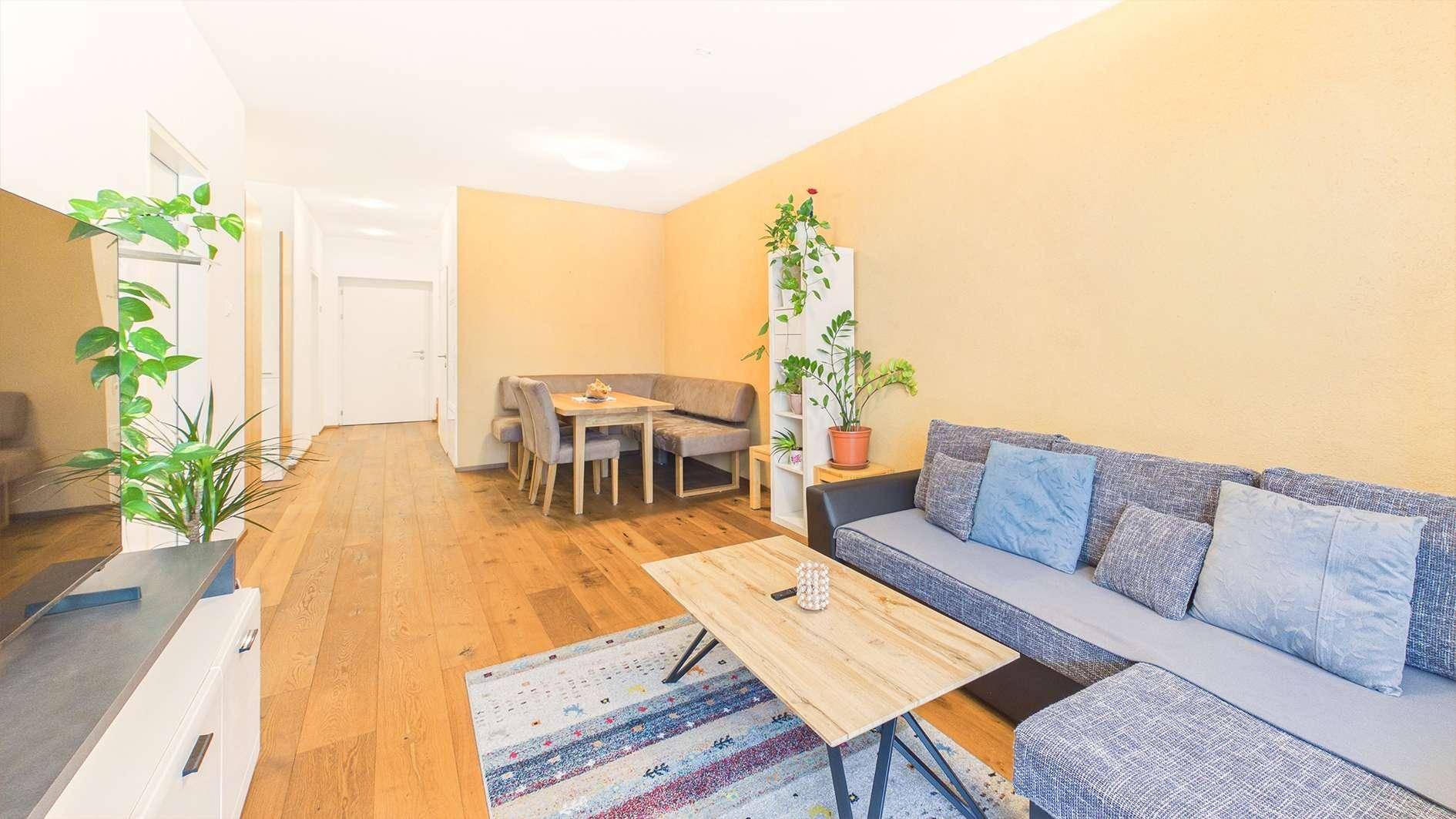 Geräumiger Wohn- und Essbereich mit Holzboden, Sofa und Pflanzen.