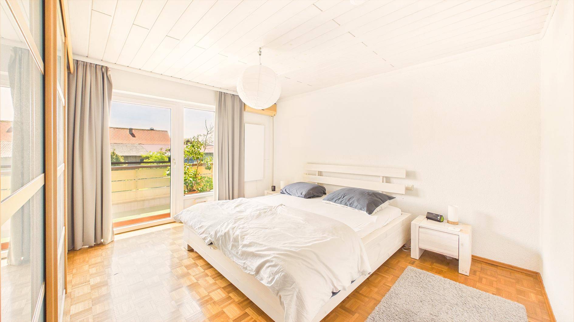 Schlafzimmer mit Parkettboden, großem Bett und Zugang zu einem sonnigen Balkon.