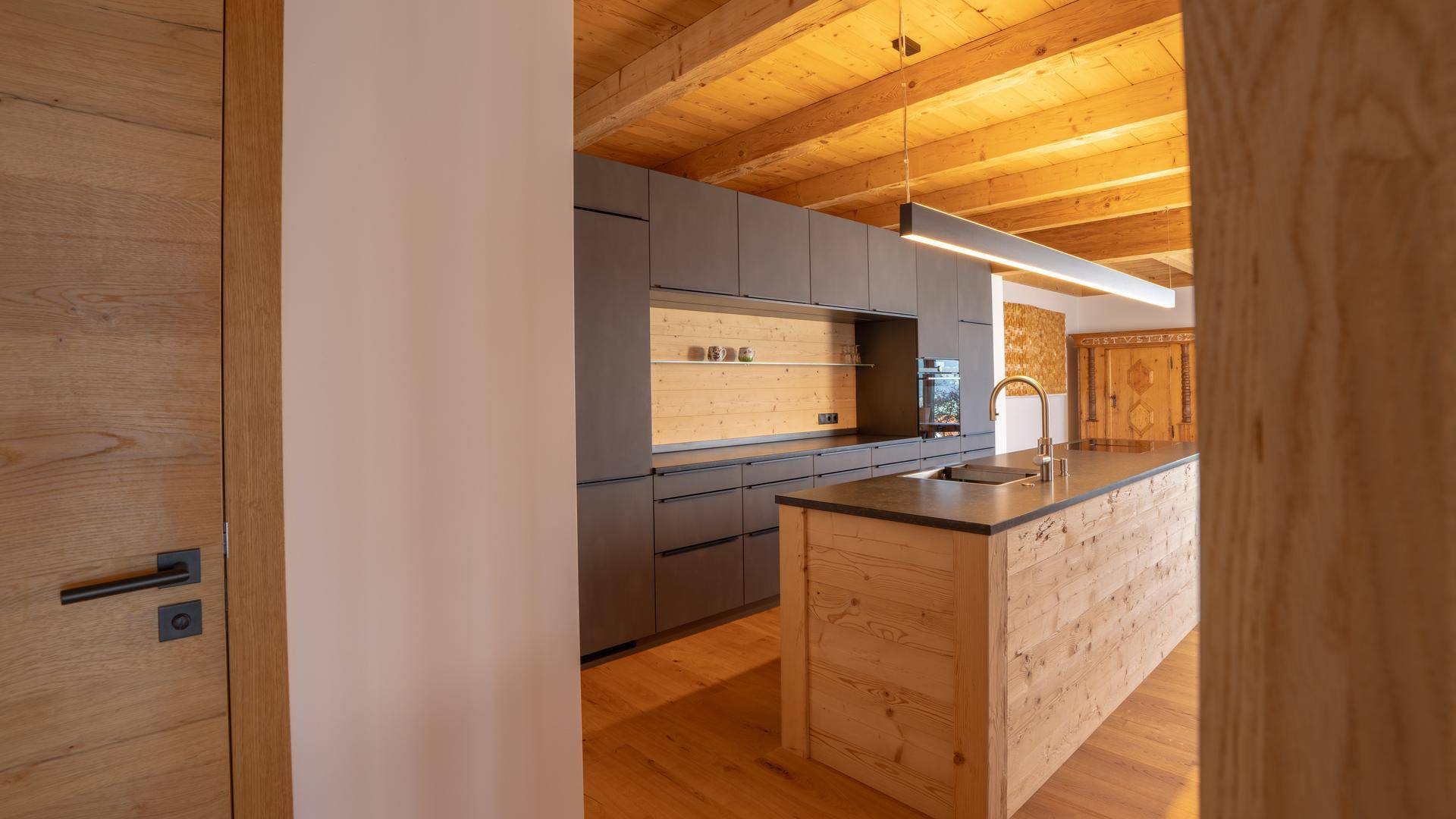 Moderne Küche mit dunklen Schränken, Holzinsel und Holzbalkendecke in offenem Design.