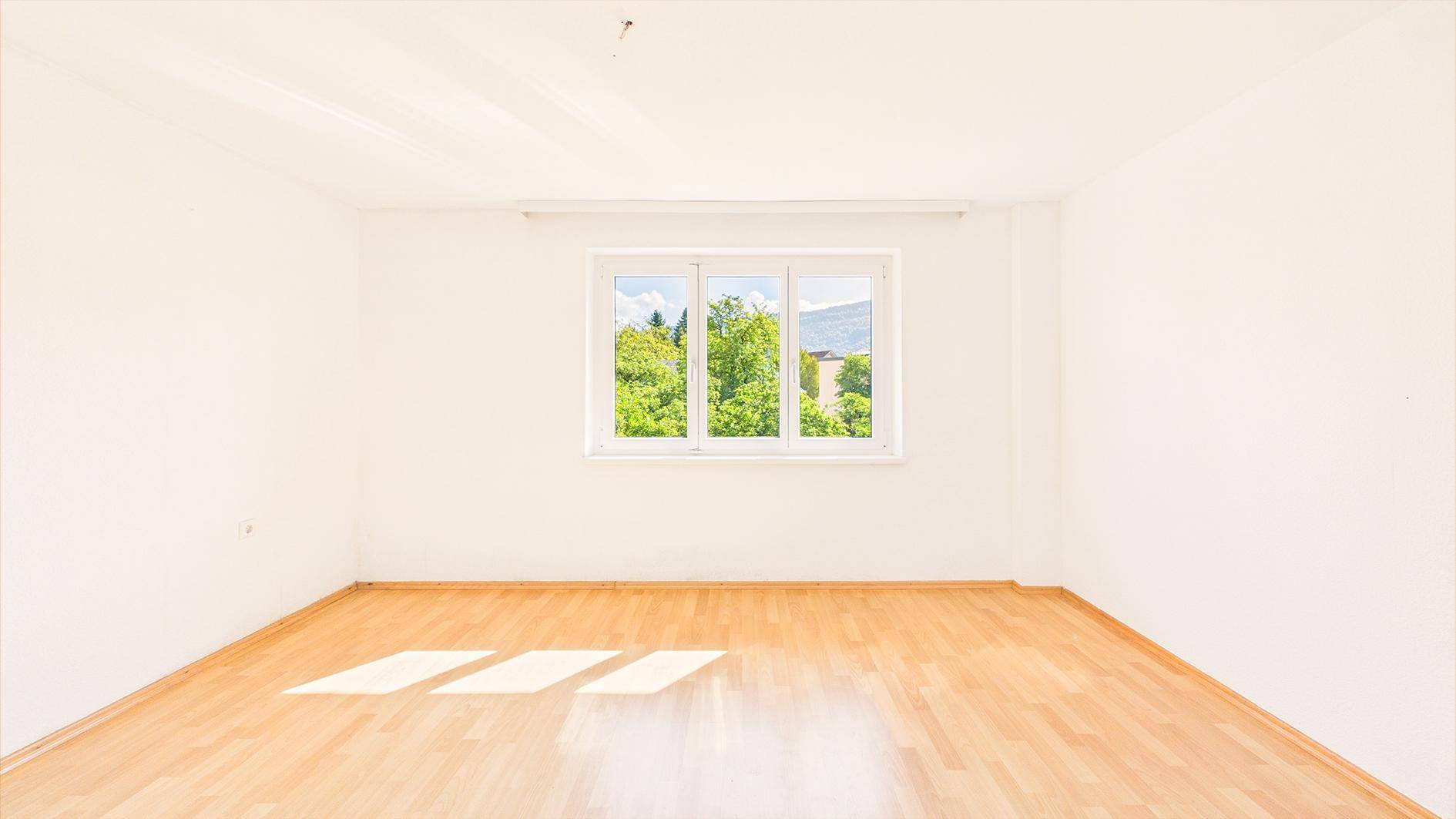 Leeres, helles Zimmer mit Parkettboden und großem Fenster, ideal als Schlafzimmer.