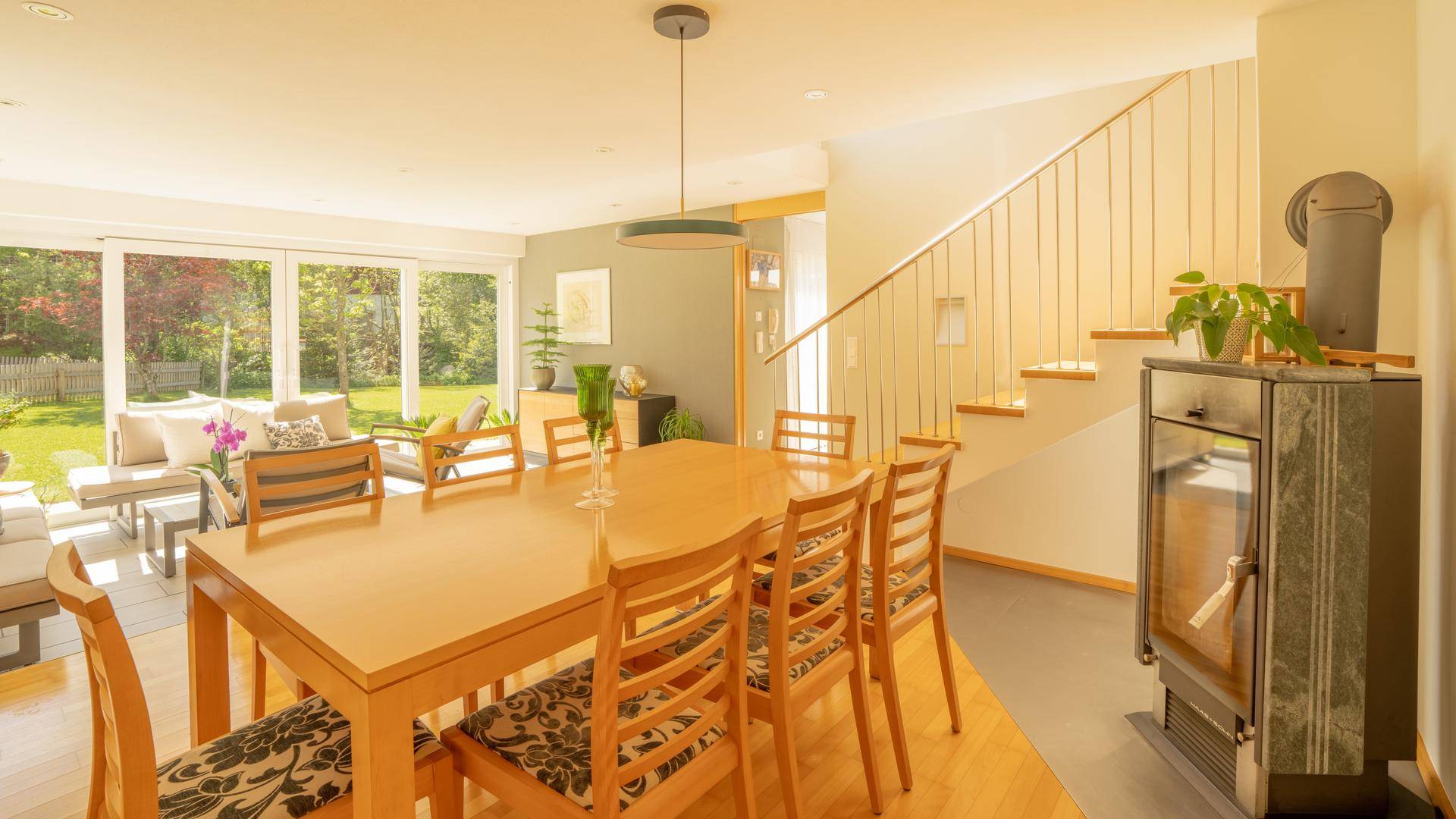 Heller Wohn-Essbereich mit Holztisch, Kaminofen und offener Treppe zum Obergeschoss.