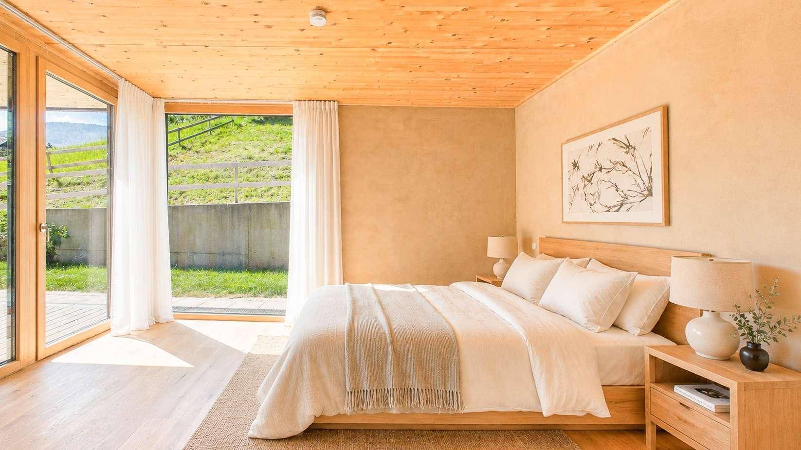 Gemütliches Schlafzimmer mit Holzboden, Holzlamellendecke und großen Fenstern, die Zugang zur Terrasse bieten.