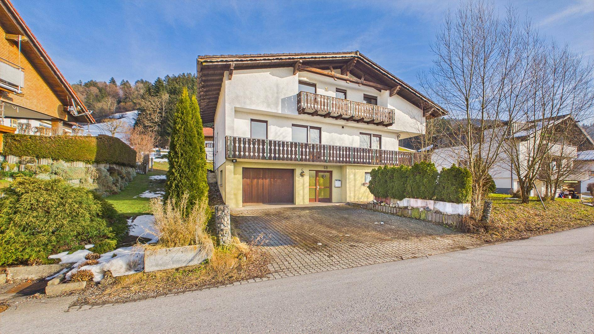 Sonniger Blick auf das traditionelle Haus mit Holzbalkonen und gepflegter Auffahrt vor Bergkulisse.
