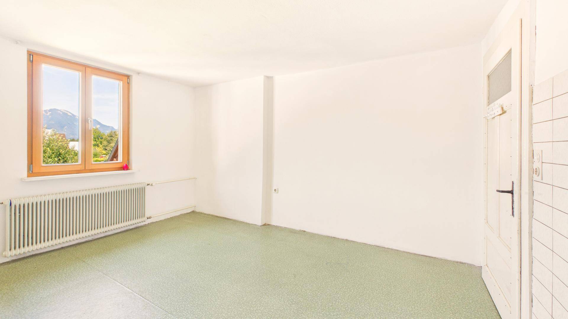 Geräumiges Zimmer mit grünem Teppichboden und Fenster mit Bergblick.