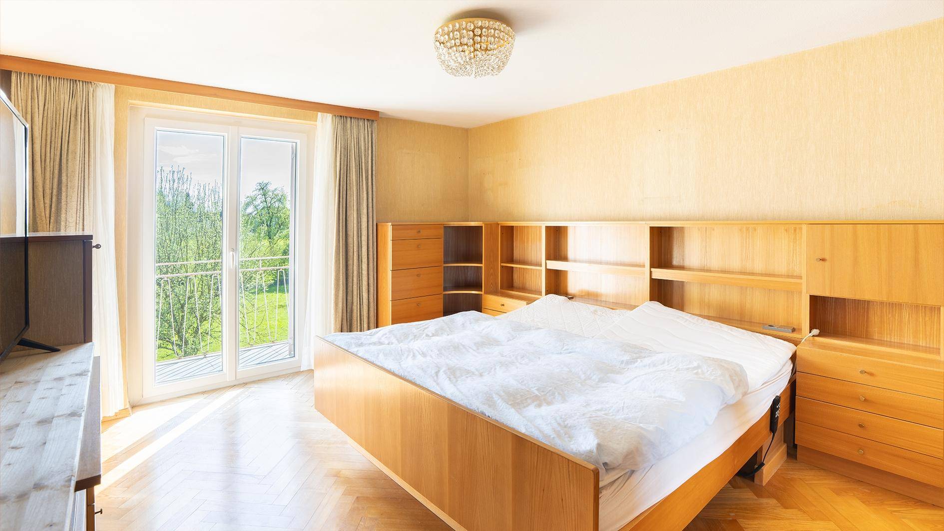 Schlafzimmer mit Doppelbett, Holzmöbeln und Balkonzugang mit Blick ins Grüne.