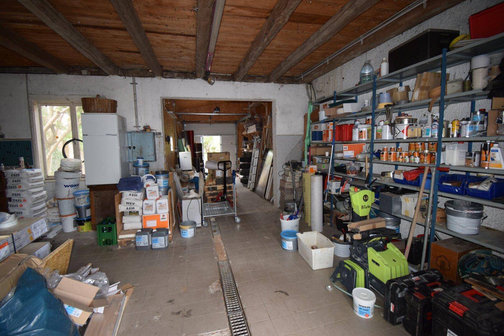 Geräumiger Werkstatt- oder Abstellraum mit Regalen, Werkzeugen und sichtbaren Holzdeckenbalken sowie Fliesenboden.