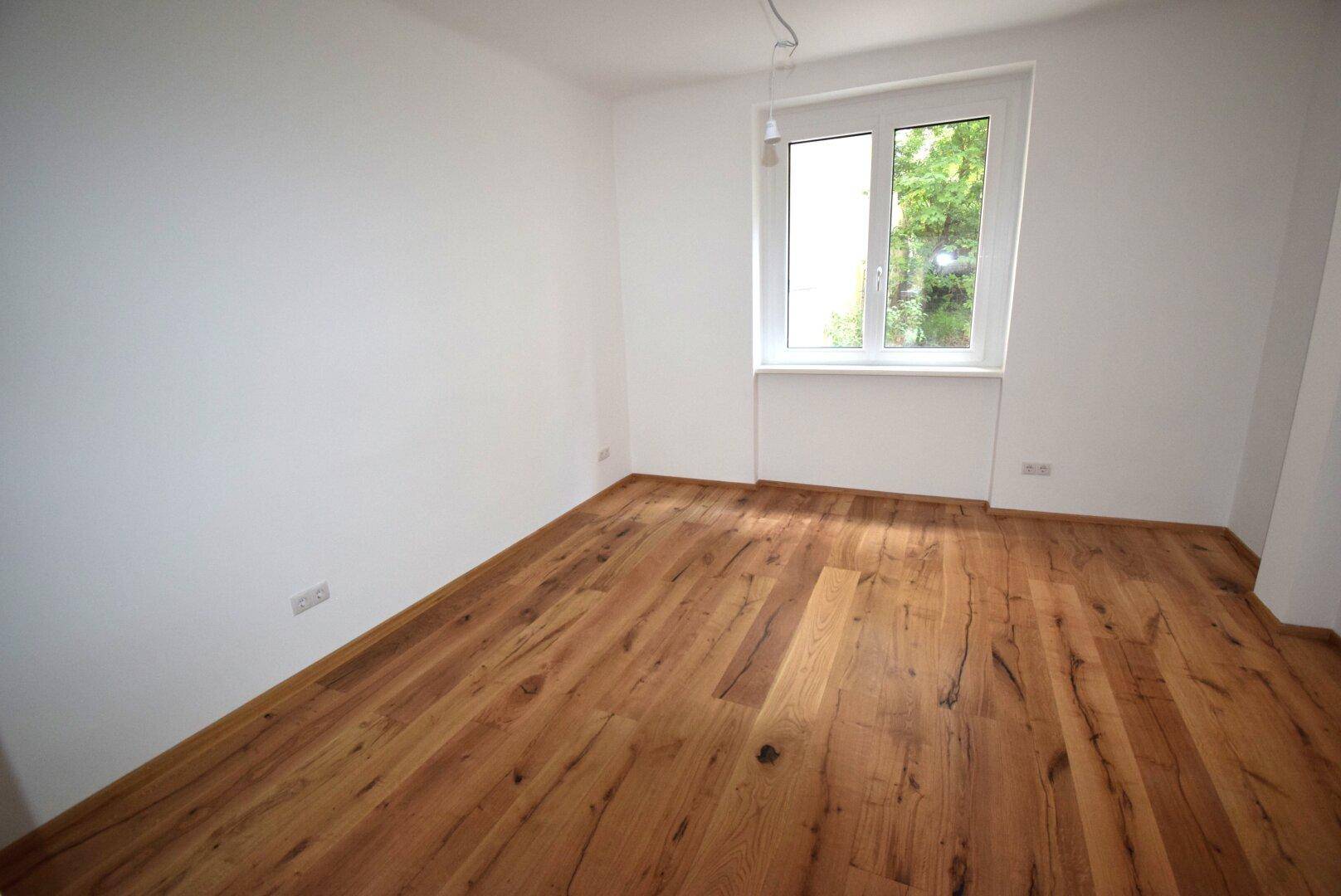 Helles, leeres Zimmer mit neuem Holzboden und einem großen Fenster.