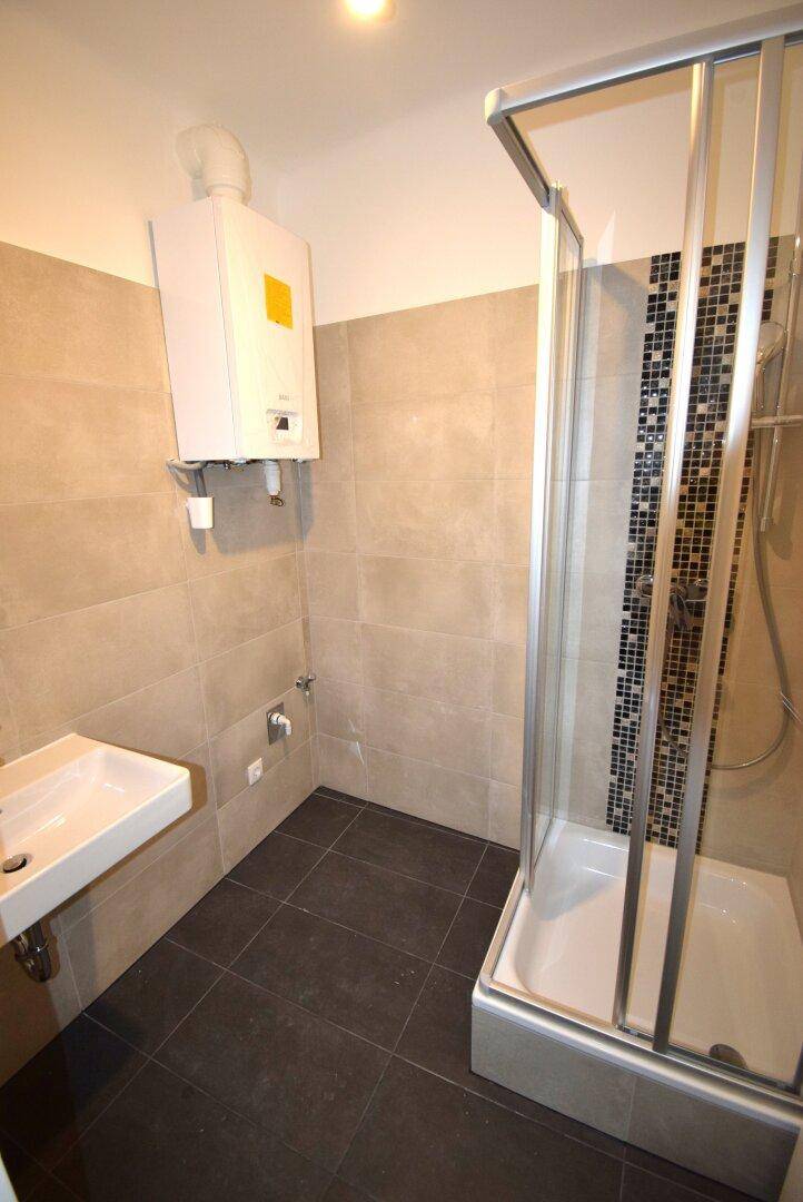 Modernes Badezimmer mit Duschkabine, Waschbecken und Gastherme an der Wand.