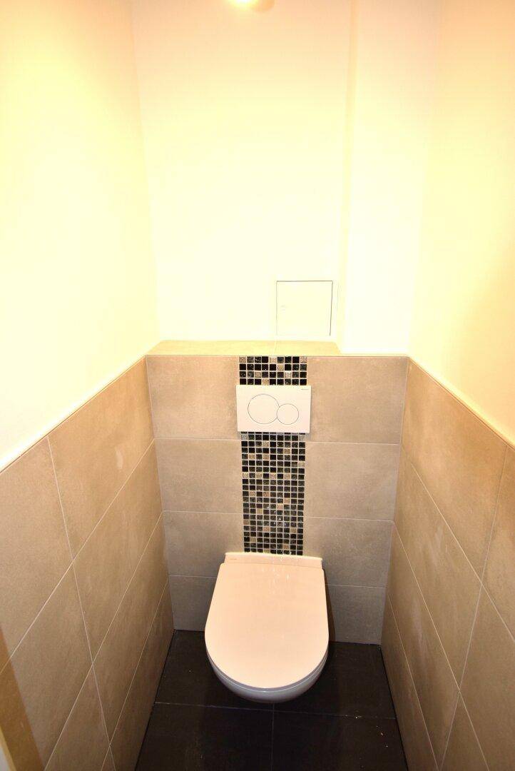Separates WC mit wandhängender Toilette und modernen Fliesen an den Wänden.