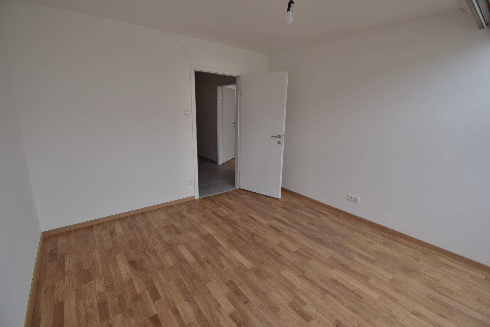 Leeres Schlafzimmer mit Parkettboden und weiß gestrichenen Wänden, bereit zur Einrichtung.