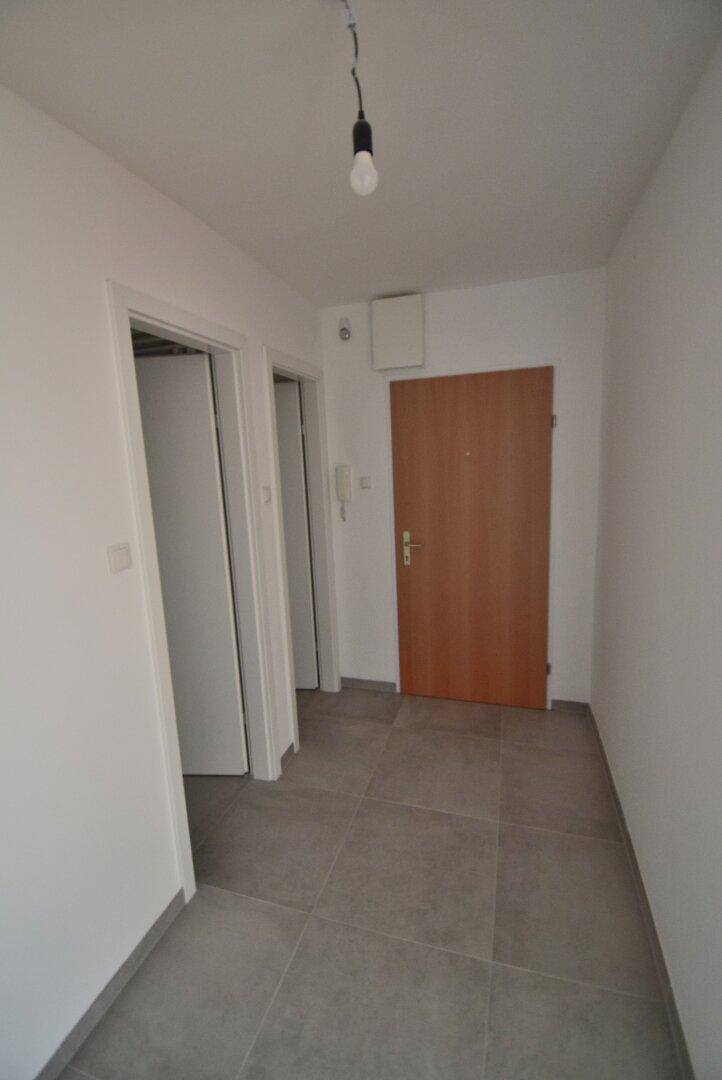 Heller Flur mit grauen Bodenfliesen und einer Holztür, die zu weiteren Räumen führt.
