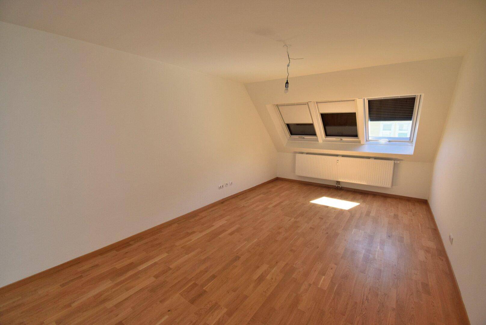 Helles Schlafzimmer mit Dachschrägen, Parkettboden und drei Dachfenstern für viel Licht.