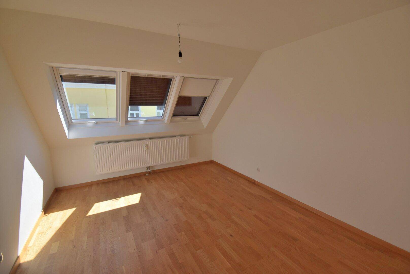 Lichtdurchflutetes Schlafzimmer im Dachgeschoss mit Holzboden und mehreren Dachfenstern.