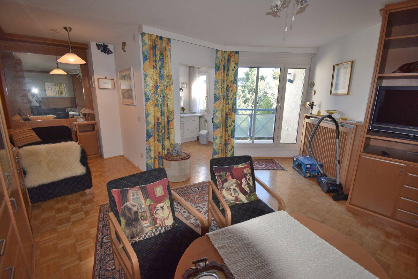 Gemütliches Wohnzimmer mit Parkettboden, Zugang zum Balkon und Blick ins Grüne.
