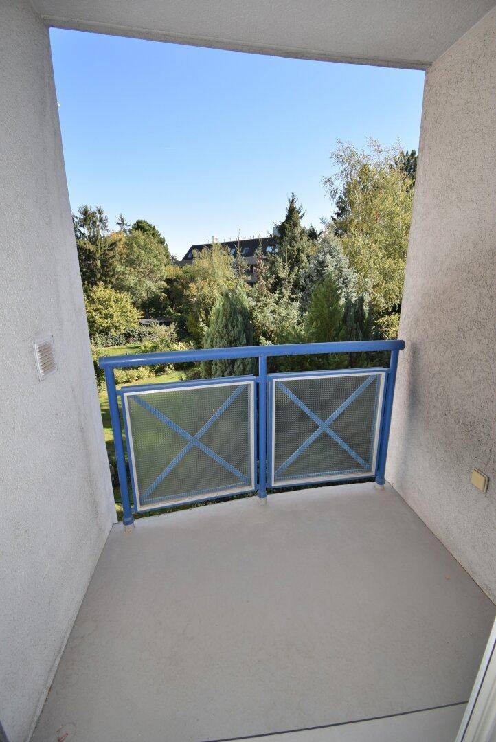 Kleiner Balkon mit blauem Geländer und Blick auf grüne Bäume.